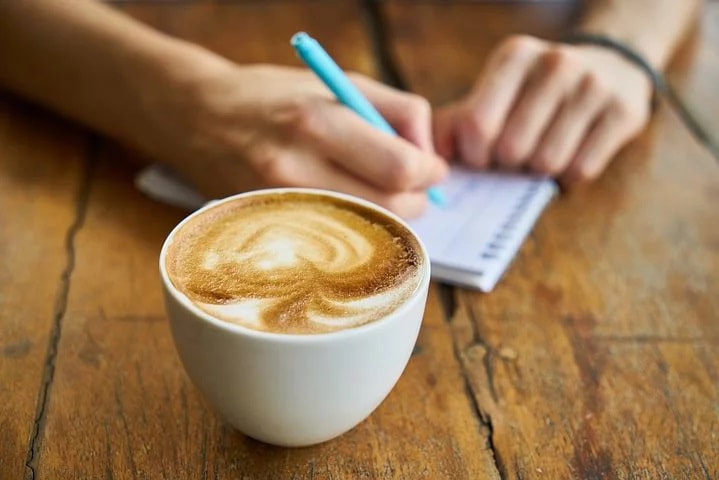 person writing on notepad with a cup of coffee