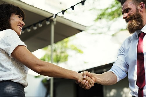 Image af a man and women dressed in work clothes smiling and shaking hands