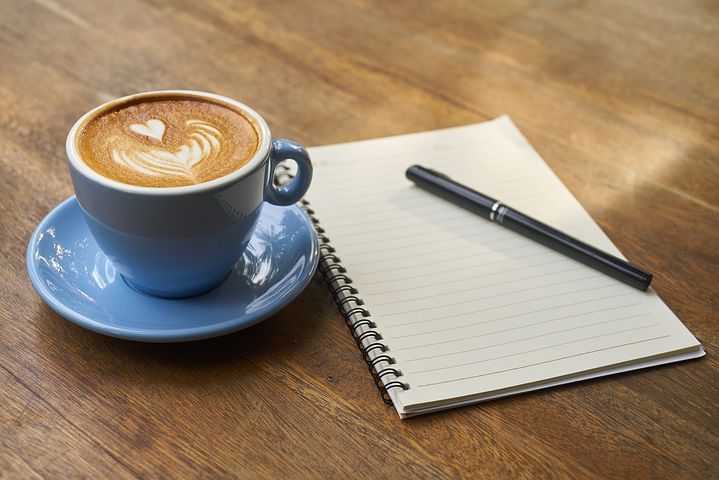 Photo of a blue coffee cup and note paper and pen on a wooden table