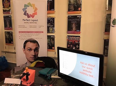 The Perfect Layout stand at the HCCI showcase event at the Queens Theatre, Hornchurch. Photo shows the Perfect Layout banner and table with television and prosecco and chocolates.