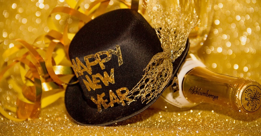 A festive scene of gold with a black hat and gold bottle of drink. on the hat is written happy new year.