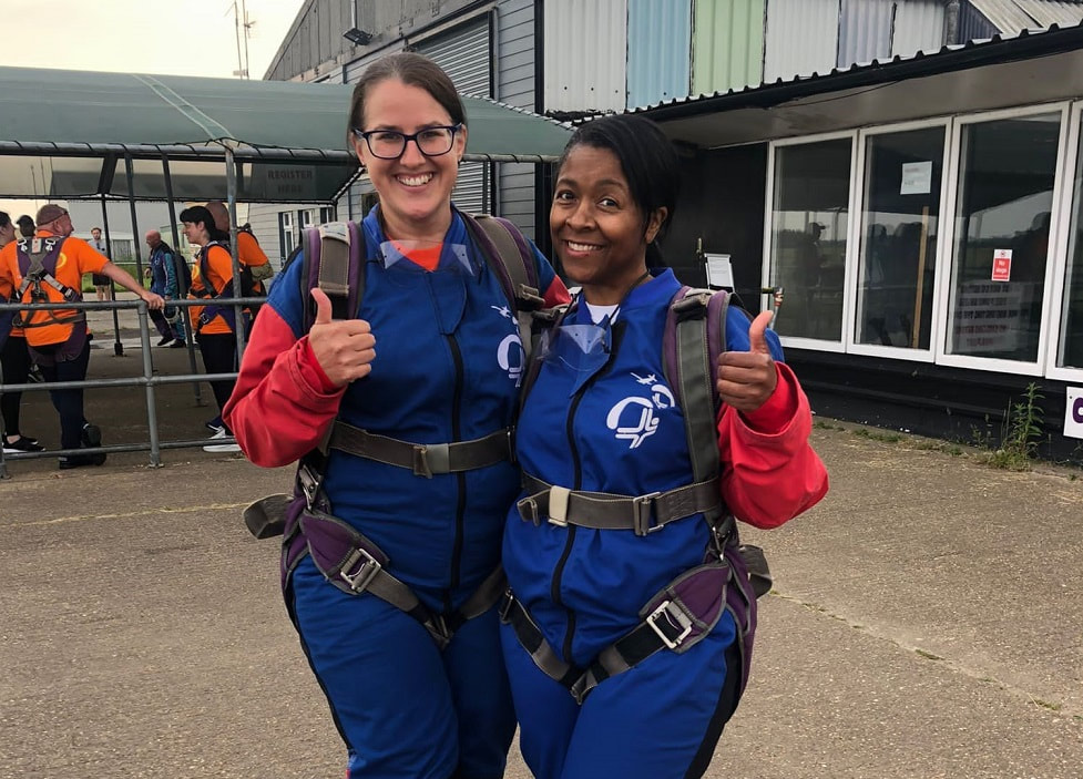 Tracey and Christine kitted up and ready to fly_smiling with thumbs up to camera_sky diving pose, smiling to camera_perfect layout jump skydive for Saint Francis Hospice