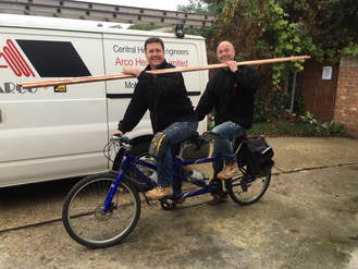 the arco team on a static tandem bike smiling holding some long copper beams