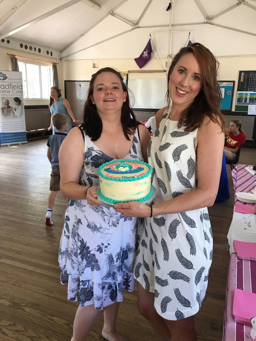 Radfield Home Care co-owners and co-directors, Lisa and Jennie wearing summer dresses holding a cake